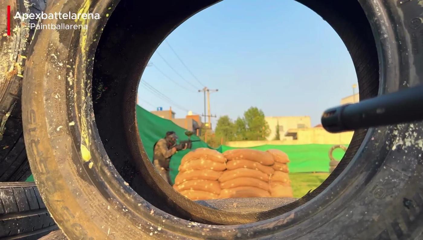 View through a stacked tyre of a player behind sandbags across the arena